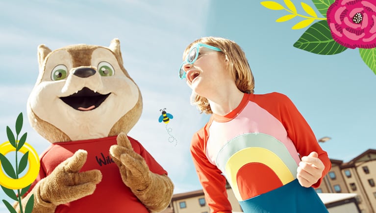 A child wearing sunglasses smiles with Wiley the Wolf at Great Wolf Lodge.